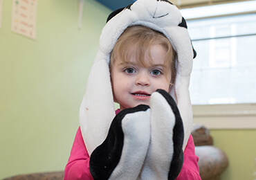 Child wearing a black and white panda hat and mittens