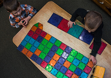 Two children playing with multi-colored magnetic tiles