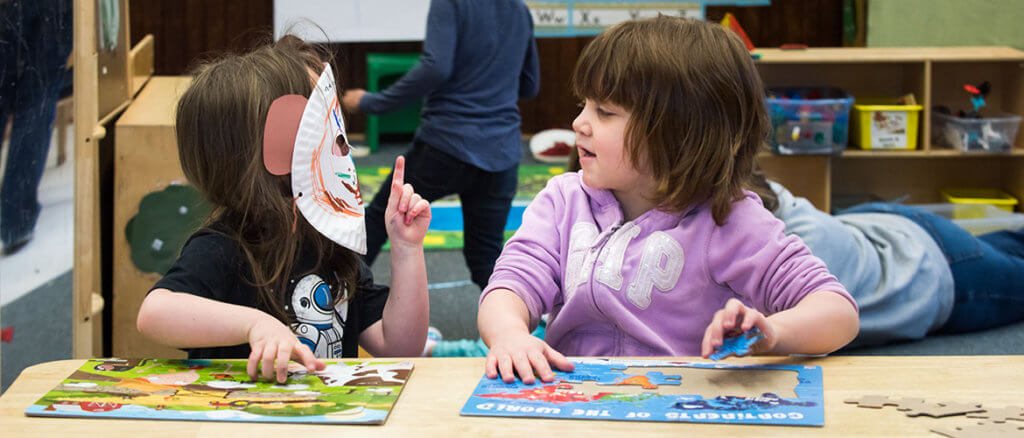 Two children sitting at a table working on puzzles