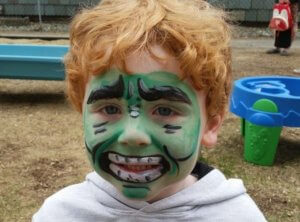 A little boy with his face painted to look like the Incredible Hulk smiles at the camera