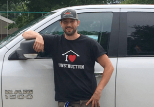 Joe stands by his truck wearing his "I love construction" shirt and cap.