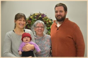 Jean poses in the center of this photo with a family and their baby in a berry hat!