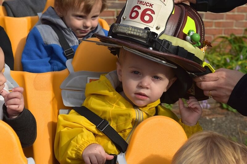 Little boy looks at the camera as he tries on a real firefighter's hat