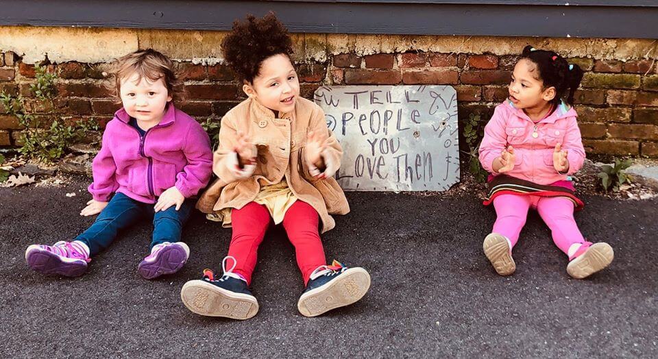 Children sitting by sign that reads "Tell people you love them"