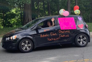 one of our teachers smiles and waves from her car which is decorated with balloons, the names of her students, and a sign that says "Ms. Casey loves you!"