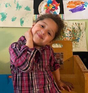 girl smiling beside a wall of art work