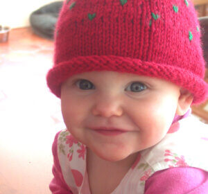 smiling baby in red knitted berry hat