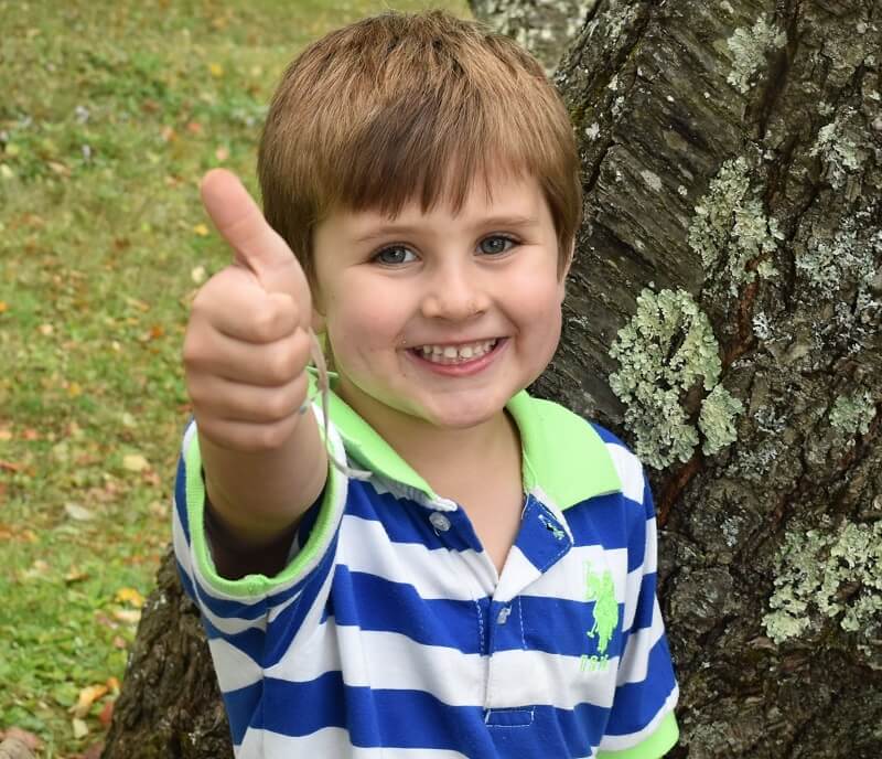child smiling and giving a thumbs up sign
