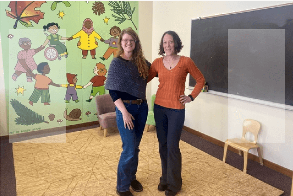 Two women standing in front of a chalkboard and mural in a room at the PCC Hub site.