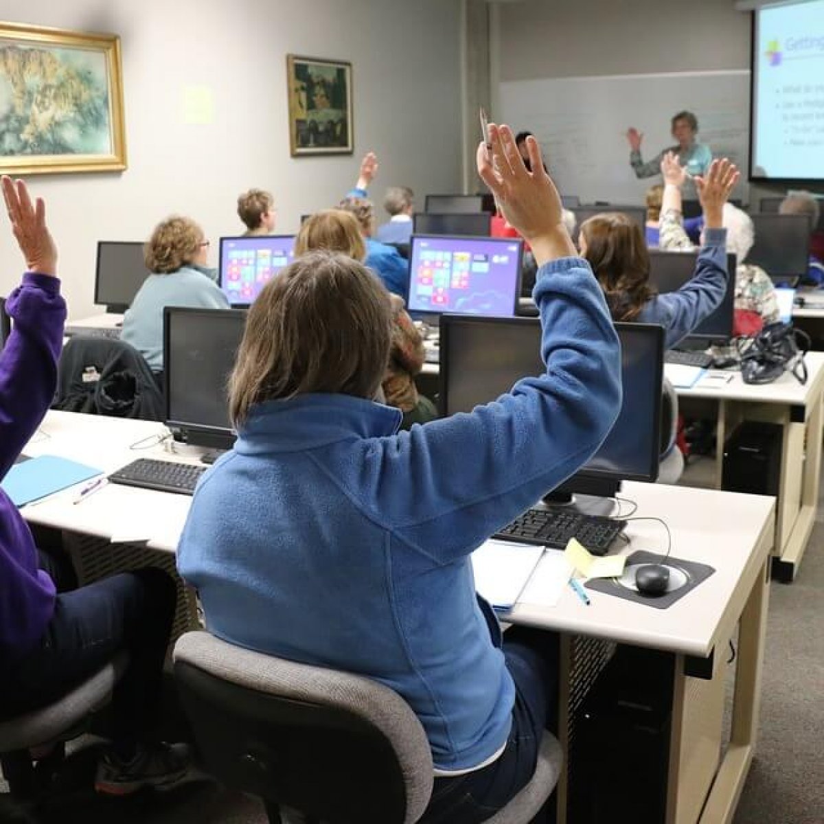 A photo of adult students seated at desks raising their hands